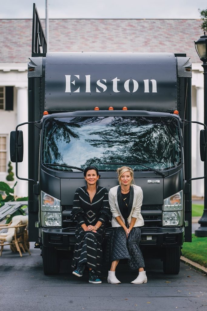 Stephanie Reynolds and Laryn Adams sitting together with the Elston Shoes mobile shoe truck behind them.