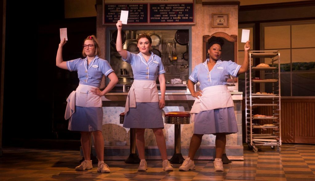 Three women  (Ephie Aardema, Christine Dwyer, and Melody A Betts) on stage holding papers as seen in the musical "Waitress"