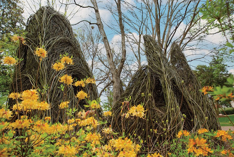 An outdoor art installation featuring straw and covered in yellow flowers located in Davidson, NC