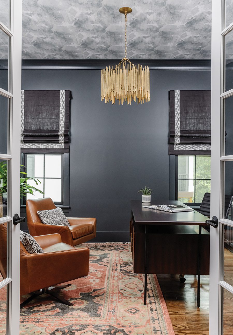 Dark gray painted room with gray curtains, a gray ceiling with an intricate gold light fixture, two brown leather chairs facing a black desk on top of an oriental rug.
