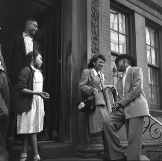 A couple in Harlem, NY leans on a railing talking while two onlookers watch circa 1946-1950