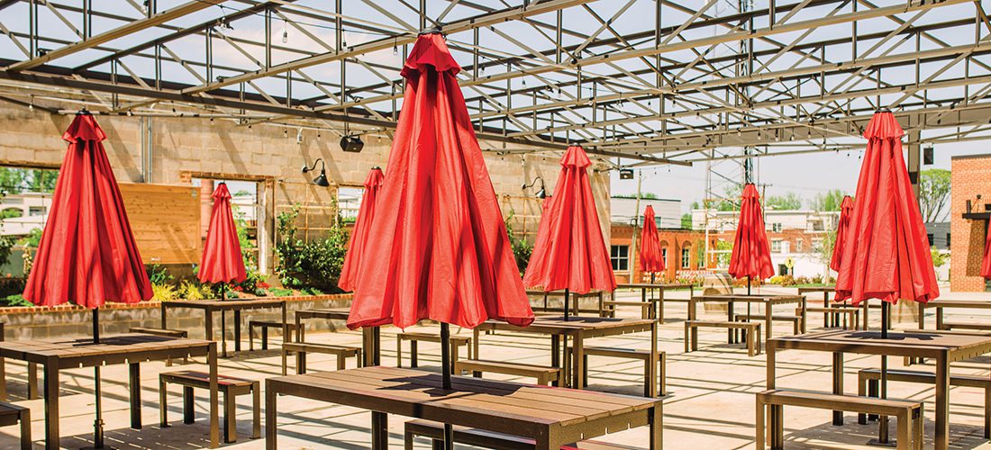 A collection of outdoor wooden tables with red umbrellas situated on the tops of each table