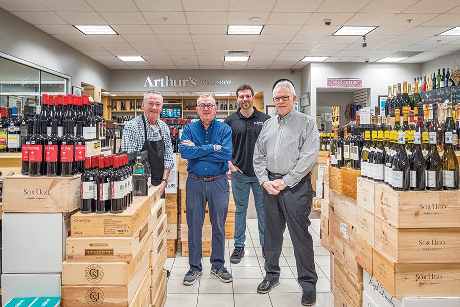 Four men stand in the middle of Arthur's Wine Shop in Charlotte, NC surrounded by cases and stacks of wine