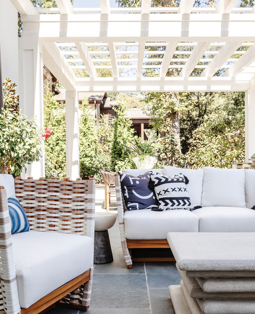 An outdoor area with white outdoor furniture, decorative pillows and a stone table designed by House of Nomad 