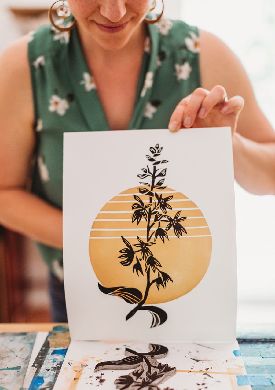 a woman reveals a print of a yellow circle with a black floral element layered on top