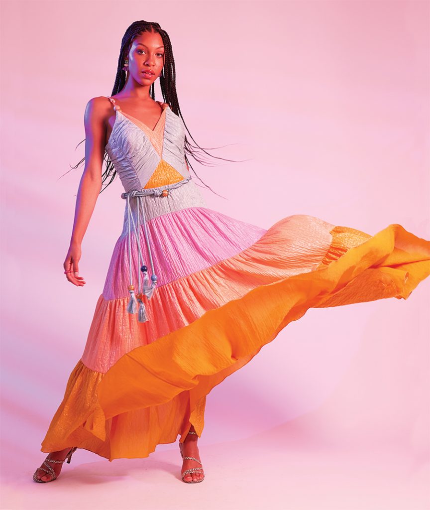 Woman stands in front of a pink background and twirls her multicolored dress