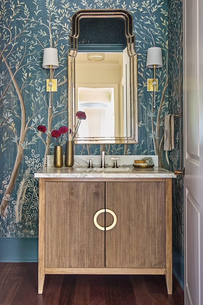 Longview home in Charlotte, North Carolina. Designed by Anne Buresh and Alair Homes. Powder room is a showstopper, featuring an elegant wallpaper with a fantastical, hand-painted design by Colette Cosentino for Schumacher. The custom vanity from Kauffman & Co. is adorned with custom Tritter Feefer hardware. The gold mirror is from Mirror Home, and the sconces are by Visual Comfort. 