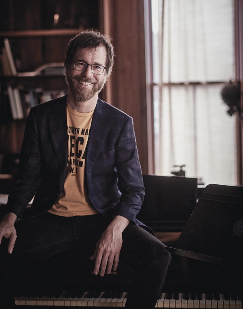 Musician Ben Folds sitting by a piano.
