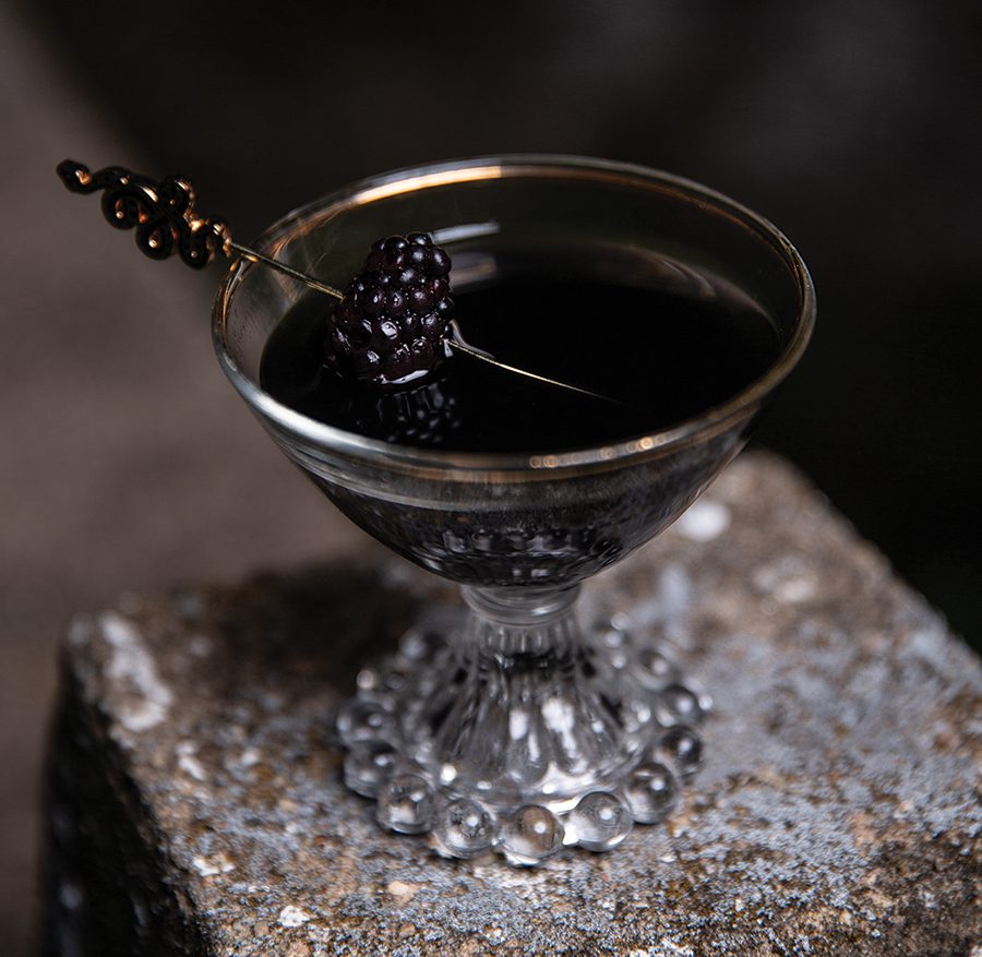 Close up photograph of the Black Viper cocktail in a decorative cup with blackberry garnish