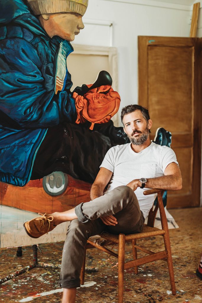 Grammy award winning musician, Scott Avett sitting on a chair in front of his large art piece of a young boy in his art studio in Concord, North Carolina. 