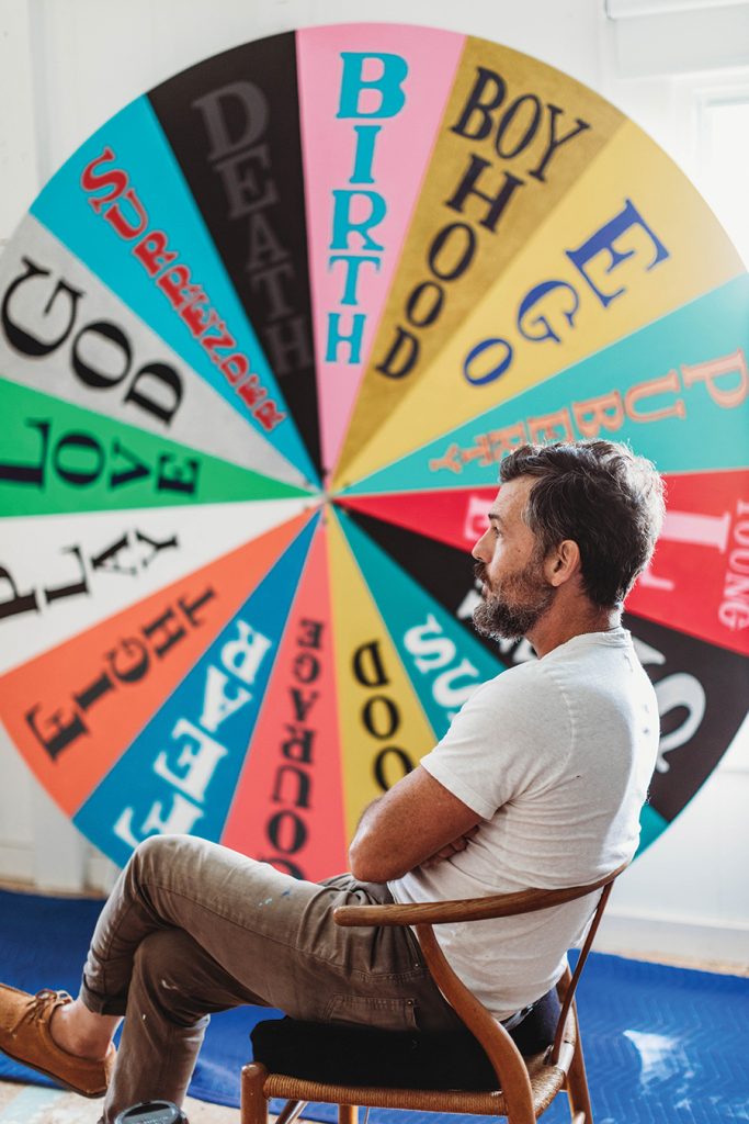 Grammy award winning musician, Scott Avett sitting on a chair in front of his circular art piece in his art studio in Concord, North Carolina. 
