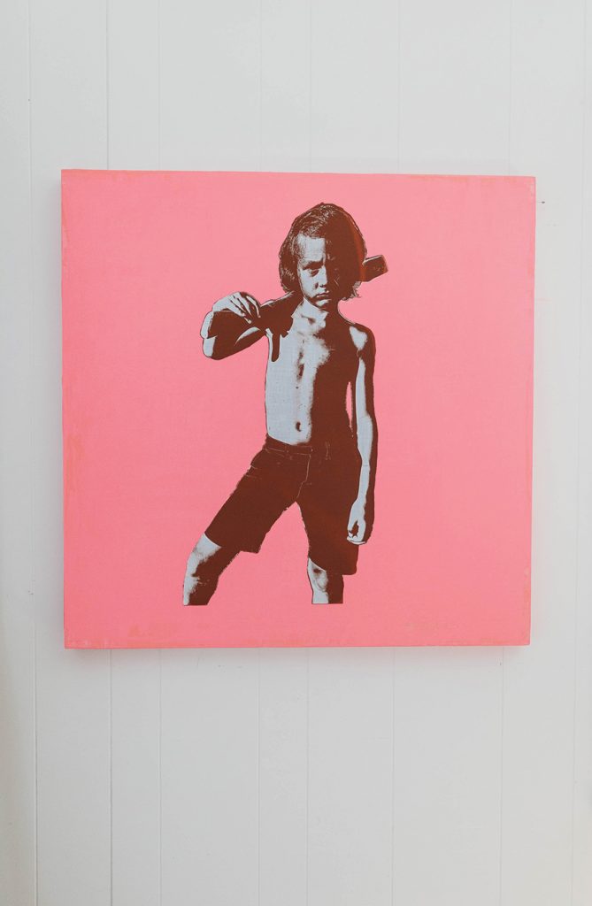 Grammy award winning musician, Scott Avett's art piece featuring a young boy with a wooden toy gun on his shoulder against a pink background. 