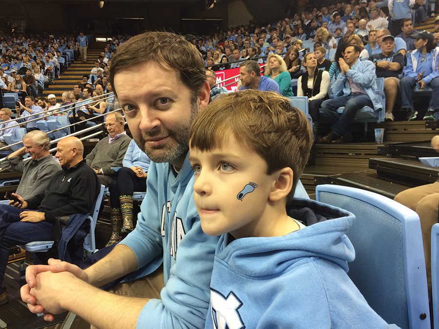 Colin and son watching the Tar Heels play basketball.