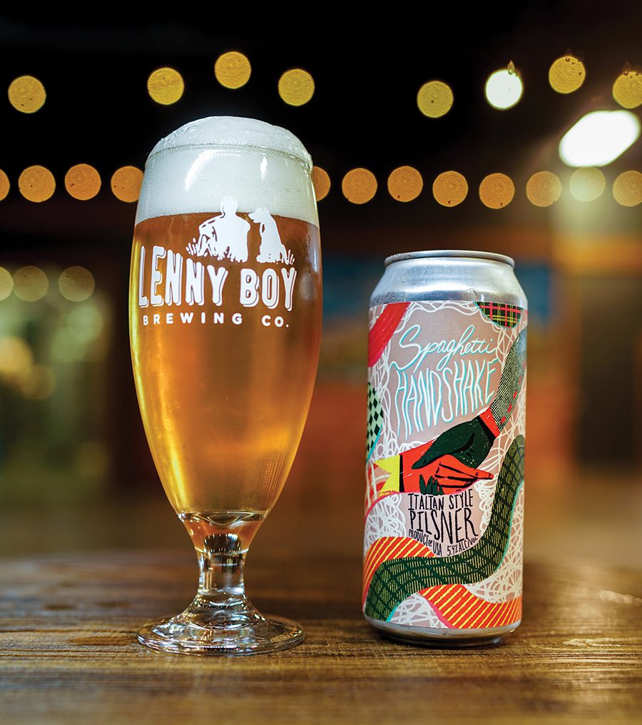 Lenny Boy Brewing Co.’s Spaghetti Handshake Hoppy Lager on table with lights in the background