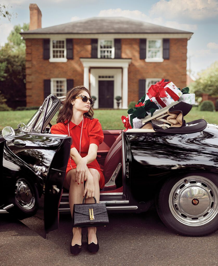 A model wears a St. John by Marie Gray vintage dress and sunglasses while sitting in a1965 Porsche 356C Cabriolet courtesy Dr. Phillip Greene; presents wrapped by Jen Gerena Design sit in the back seat. 