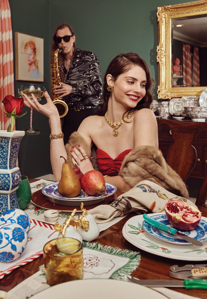 A holiday style photo shoot for SouthPark Magazine shows a model in a red dress sitting at table with festive decor.