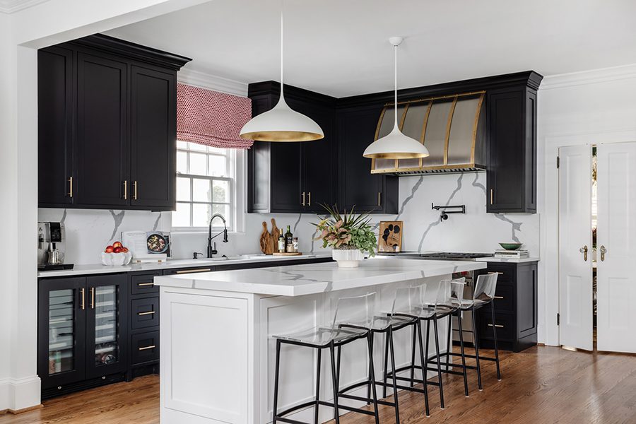 A custom metal hood is a focal point in the black-and-white kitchen. Visual Comfort “Agnes” pendants hang above the island in this Myers Park home designed by Shadie Copeland.