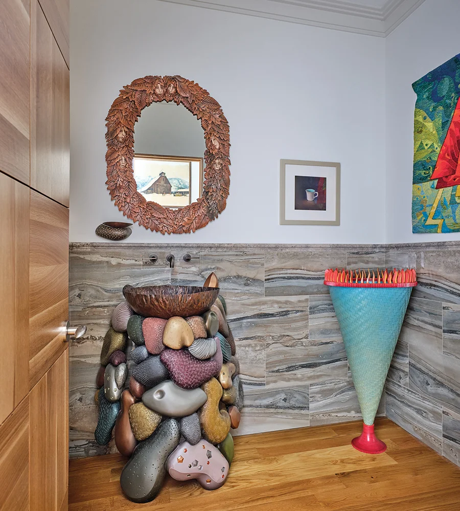 In the powder room, the sink basin by metal artist Julia Woodman sits atop a wood base by Brent Skidmore from Asheville. The mirror is by Becky Gray. A painting by Charlotte artist Christopher Clamp is displayed above a sculpture by John Skau.