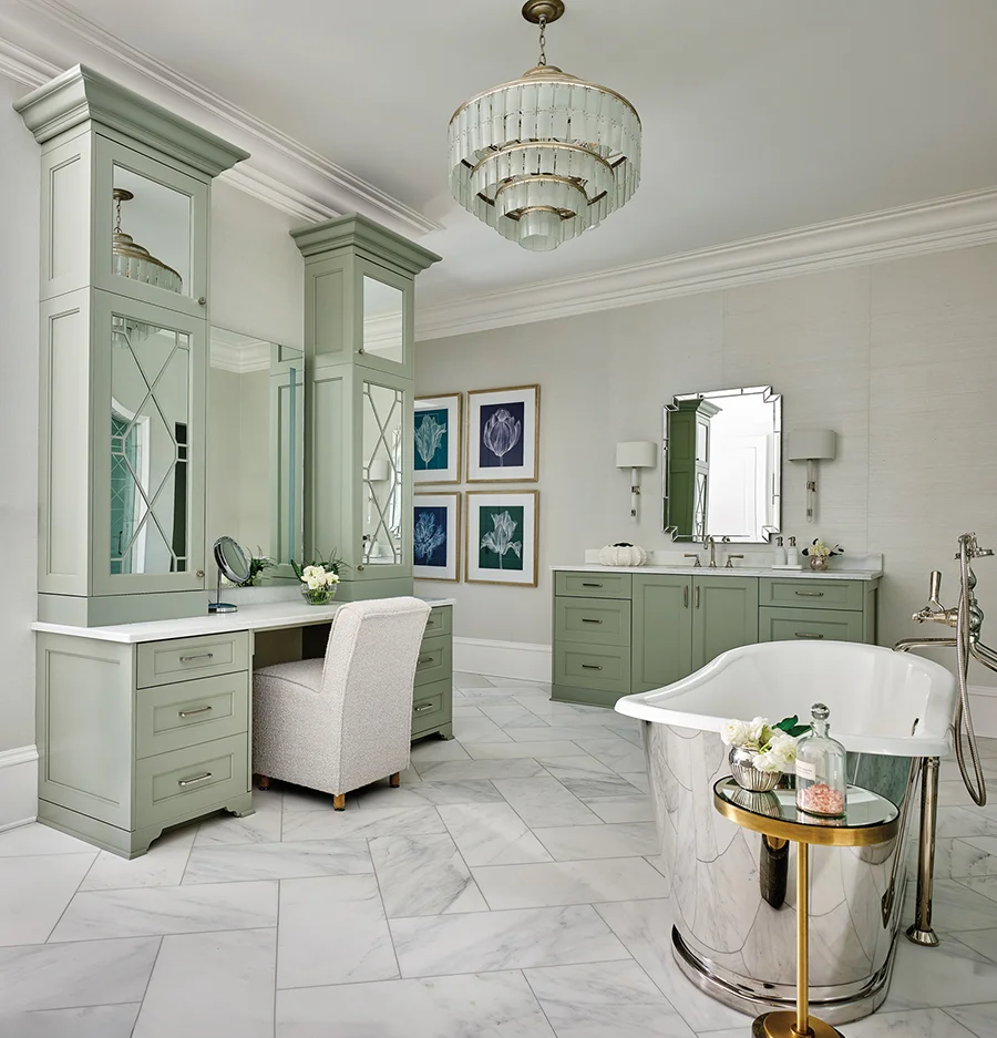 A Currey & Company chandelier hangs in the bathroom, where cabinets are painted a soft sage green to create a soothing, spa-like atmosphere.