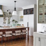 Wrought-iron stools by Arteriors flank the kitchen island, which is illuminated by Visual Comfort pendant lights. The wet bar, opposite, features an ice maker and under-cabinet refrigerator for casual entertaining