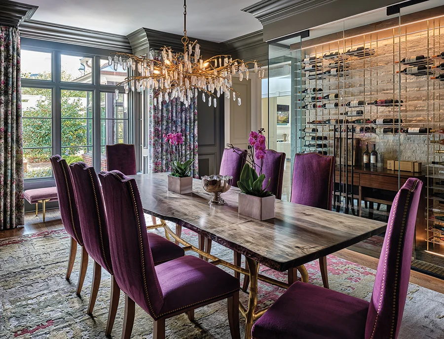 The custom wooden slab dining table is surrounded by Made Good chairs, upholstered in an aubergine velvet. The crystal quartz chandelier is by Currey & Company. An enclosed refrigerated wine storage system lines the wall.