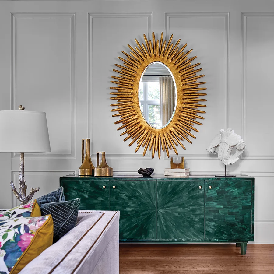 An emerald green faux-horn sideboard and gold starburst mirror by Made Goods accent a wall in the living room.