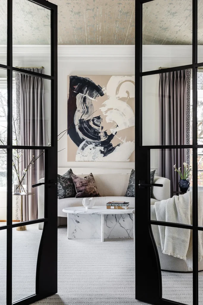 Large steel doors by Clark Hall mark the entrance to the living room, where an abstract painting by the homeowner’s mother hangs above the sofa. Nobilis’ Fresco wallpaper adds texture on the ceiling. The coffee table is by Burke Decor.