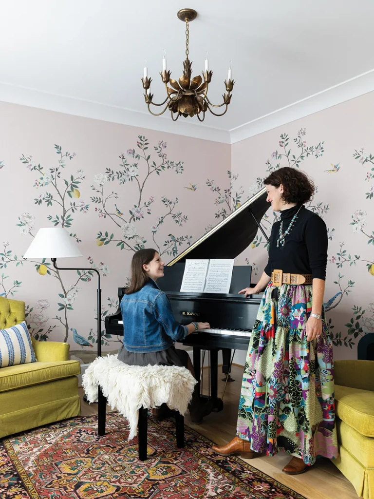 Daughter Olivia plays the piano, bought on Facebook Marketplace along with the rug. She found the green chairs through a Facebook group, and the mural wallpaper is from Anthropologie.