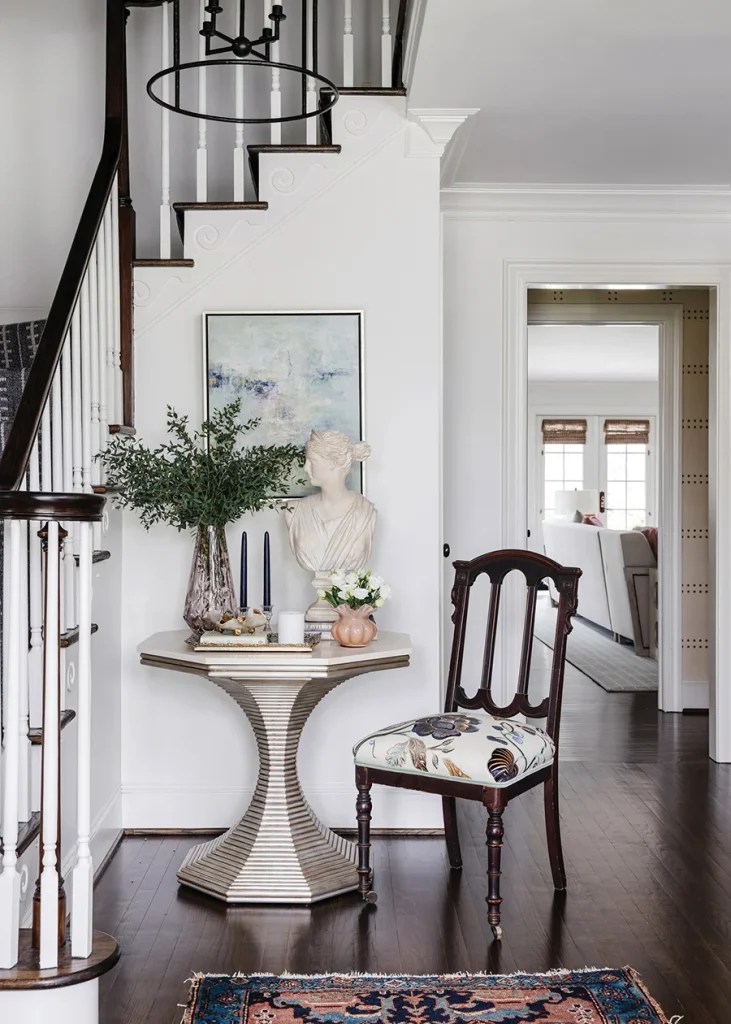 In the entry hall, antique chairs were reupholstered in an embroidered velvet fabric. The antique rug is a family heirloom; the hourglass table is by Bunny Williams.